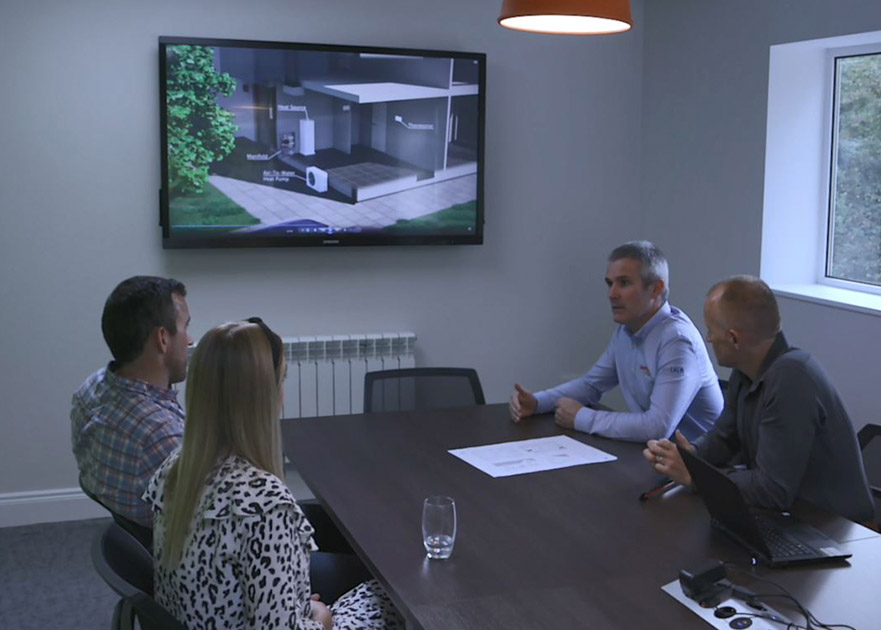 two customers having a meeting with the Pipelife team with diagram of air to water heating on a screen on the wall