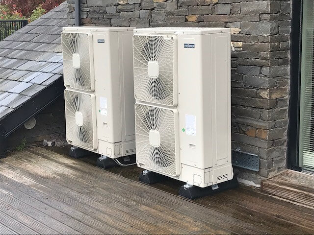 two heat pumps next to a brick wall