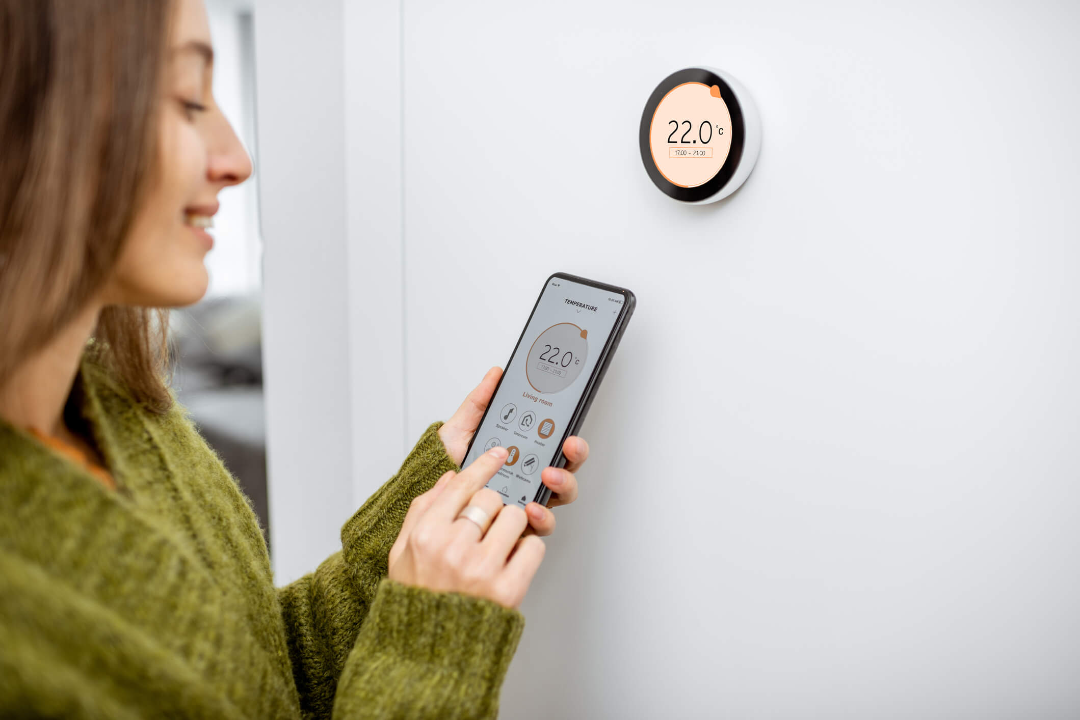woman adjusting smart thermostat using her phone