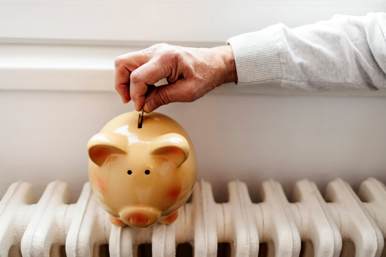 man putting coins into a piggy bank on top of a radiator to represent energy saving concept