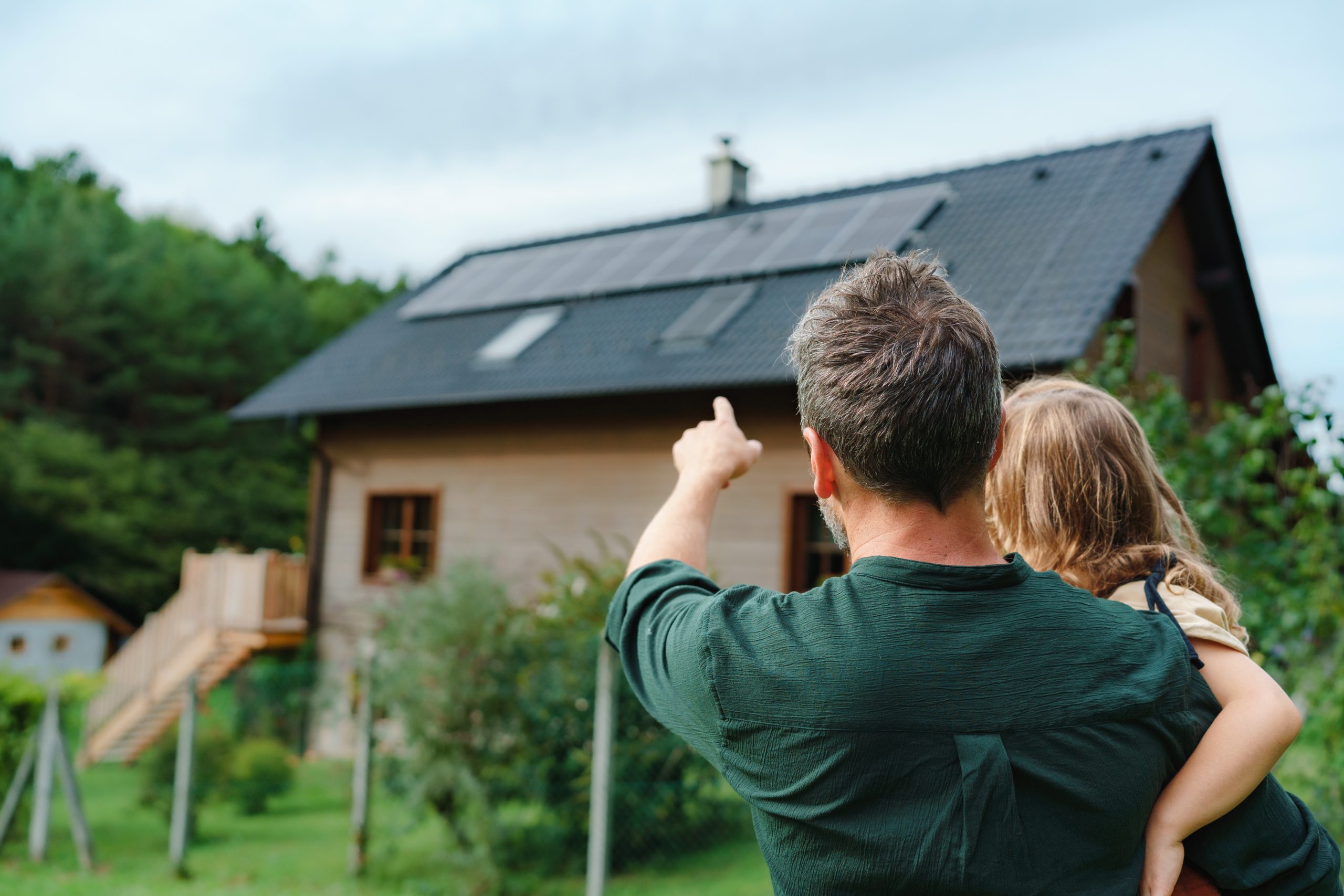 dad holding child pointing at a house with solar panels